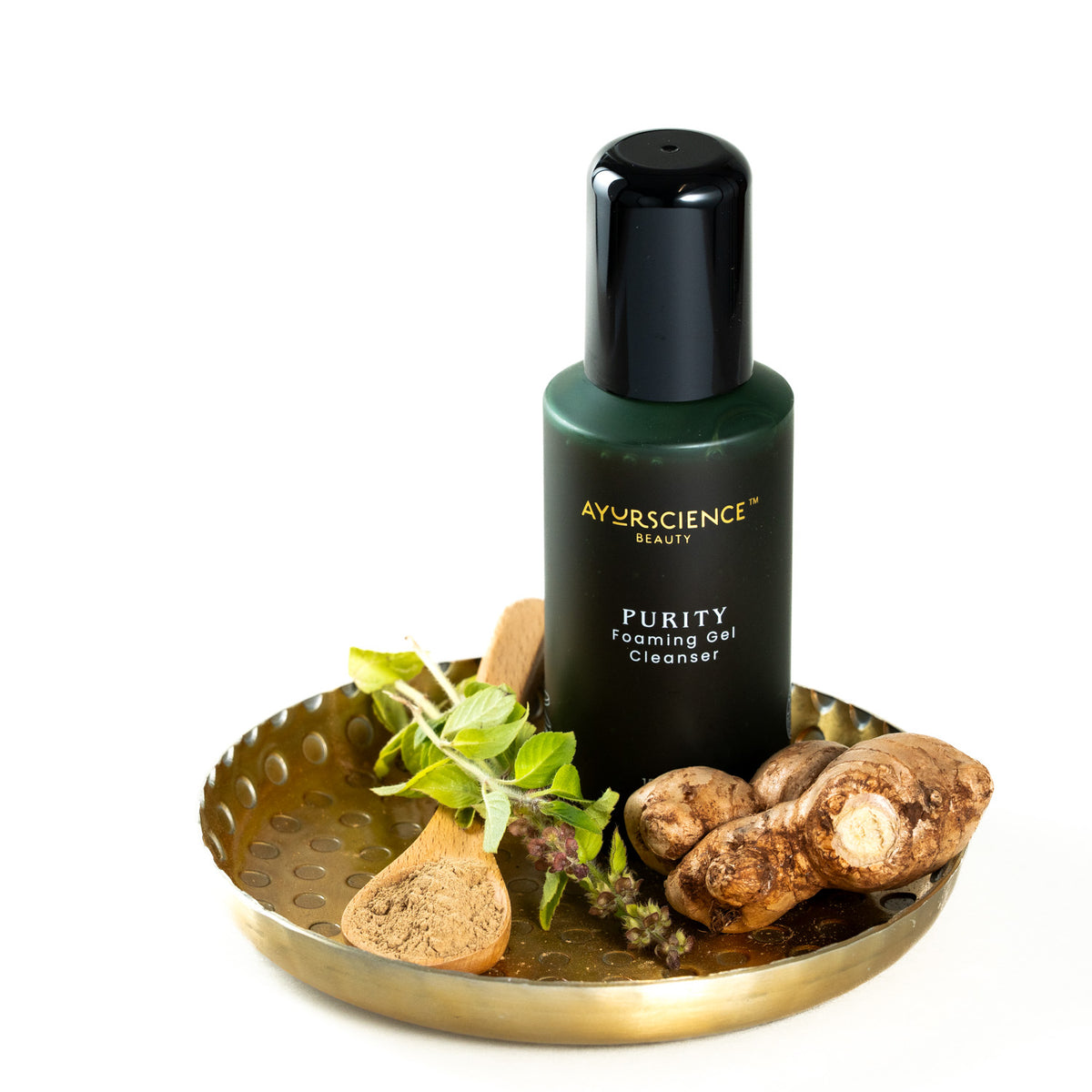 AyurScience Beauty purity foaming gel cleanser bottle on brass plate with example of herbs, tulsi and powder and ginger. Herbal skincare.
